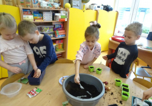 Dzieci nasypują łyżkami ziemię do doniczek.